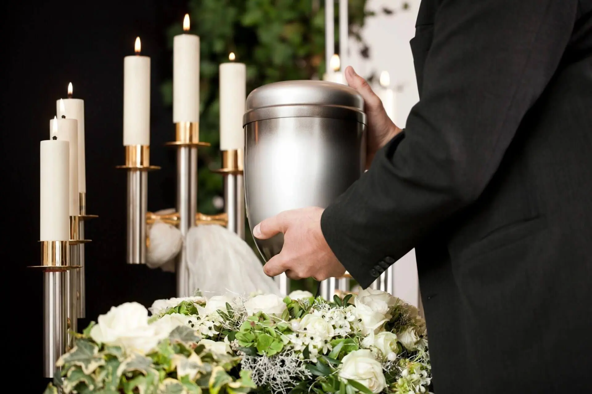 Person holding a silver urn with candles and flowers.