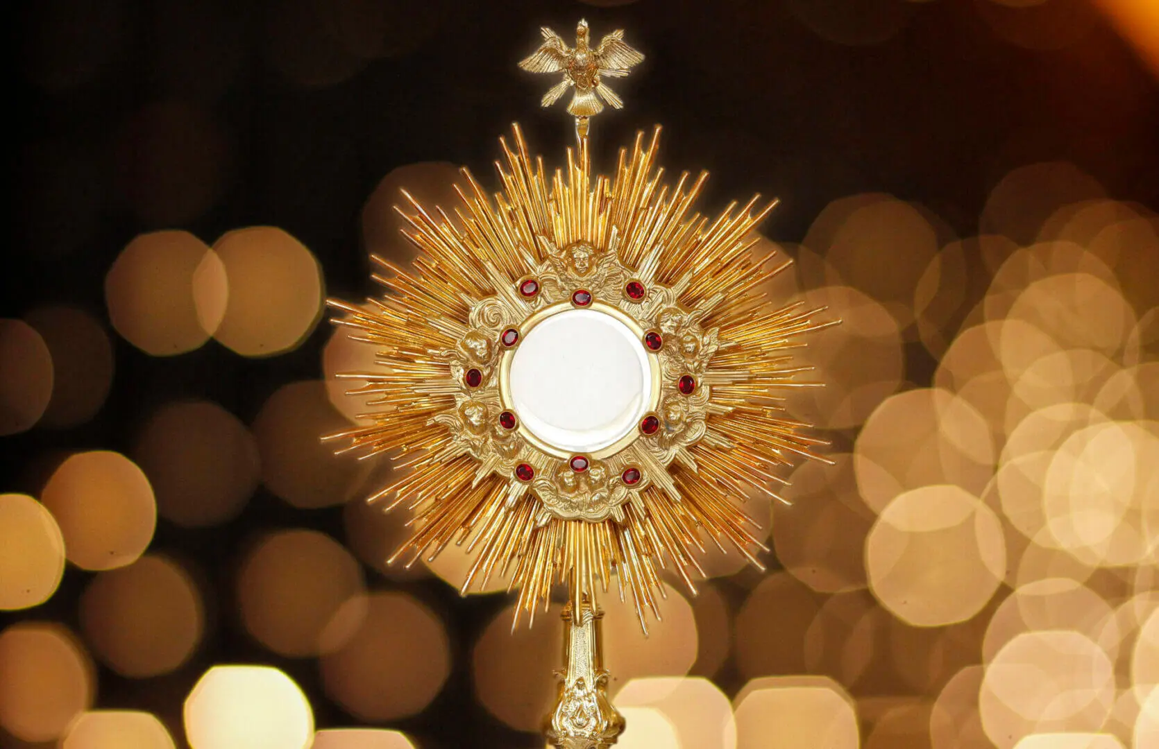 Golden monstrance with red jewels and a dove.