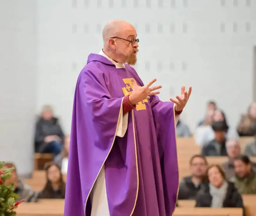 A priest in purple robes addressing a crowd.