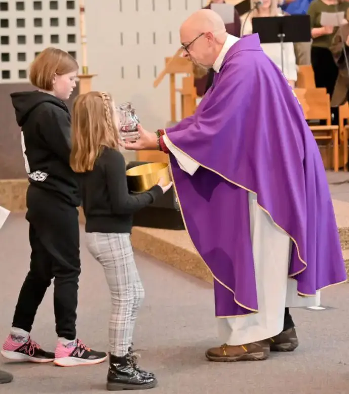 Priest giving communion to two young girls.