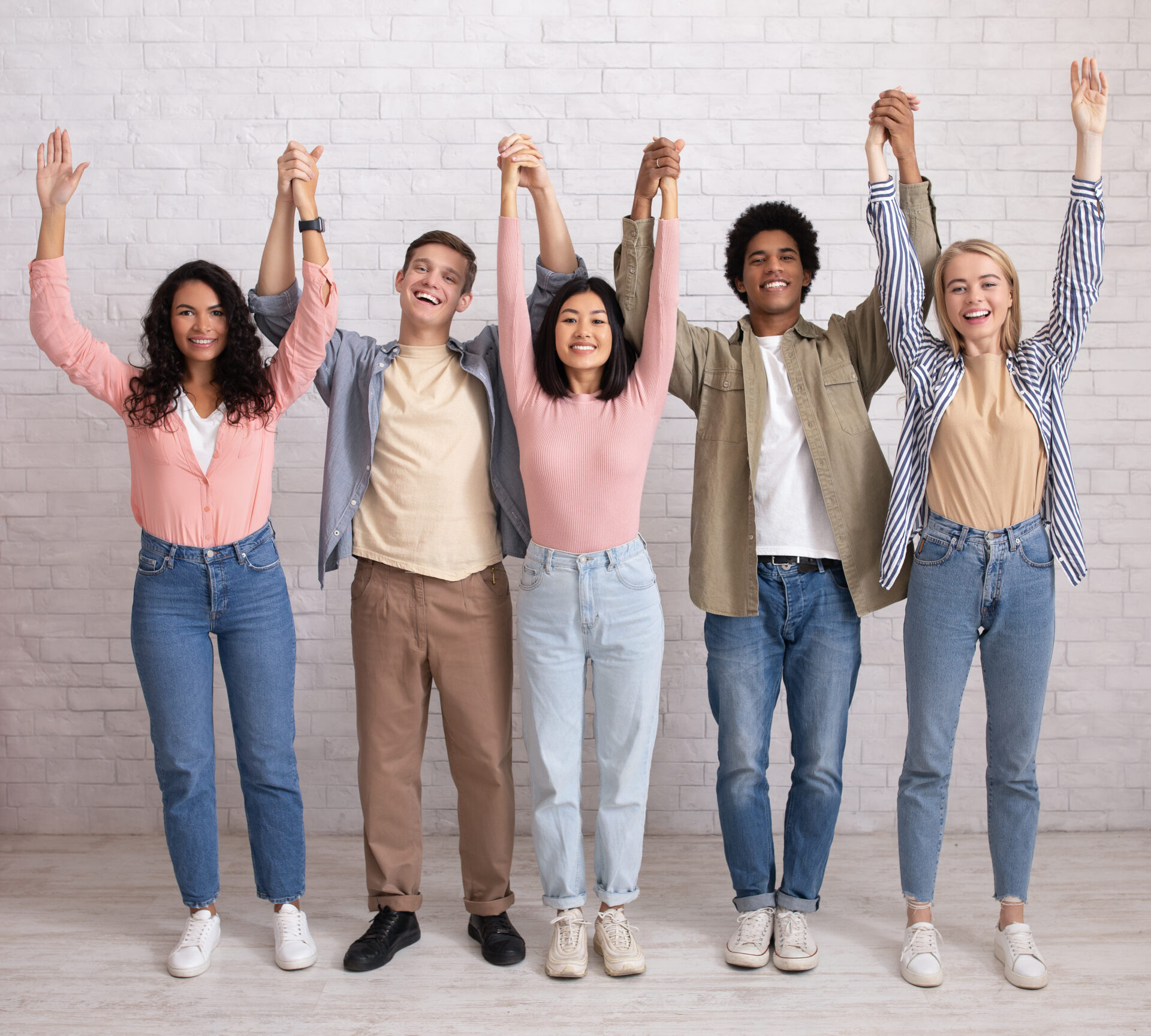 Teamwork, support from friend in studies and emotions of success. Cheerful digital young international people hold hands and lift up and have fun, on white wall background, studio shot, empty space