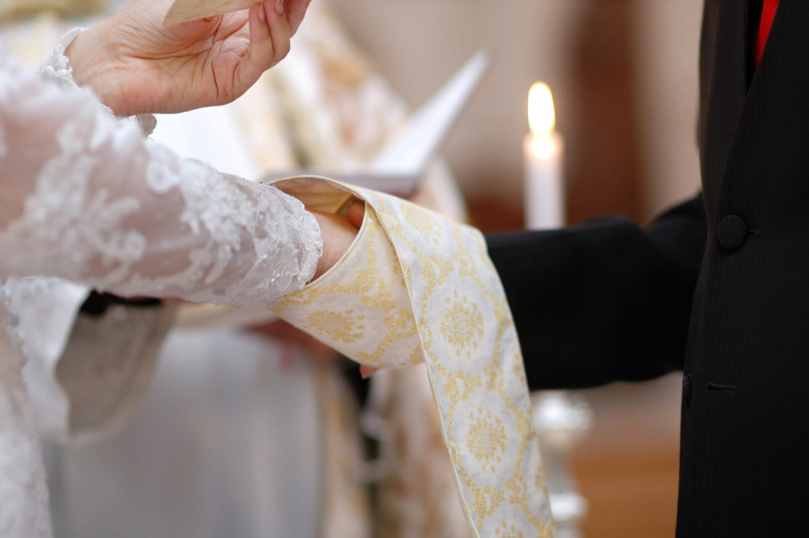 Wedding: bride and groom's hands wrapped in priest's cassock
