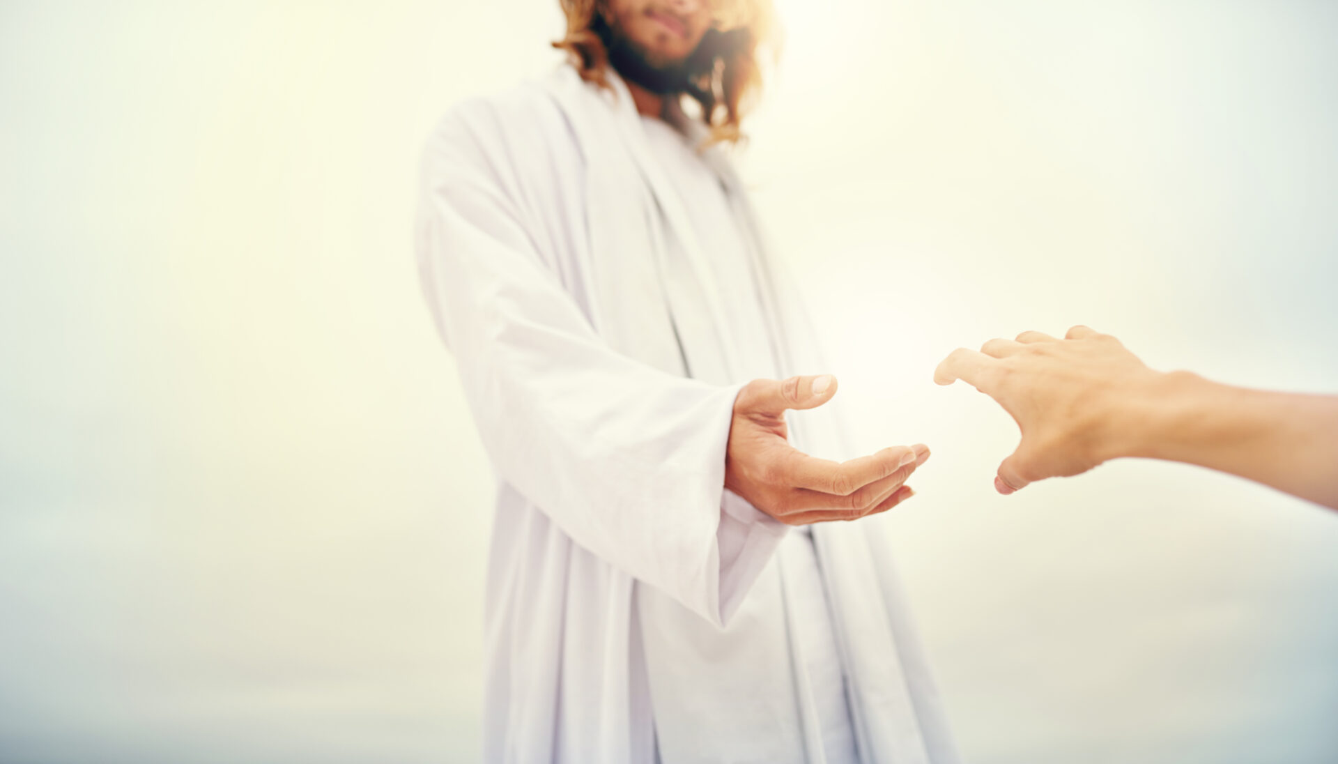 Shot of Jesus standing with his hand outstretched toward a follower on a bare landscape