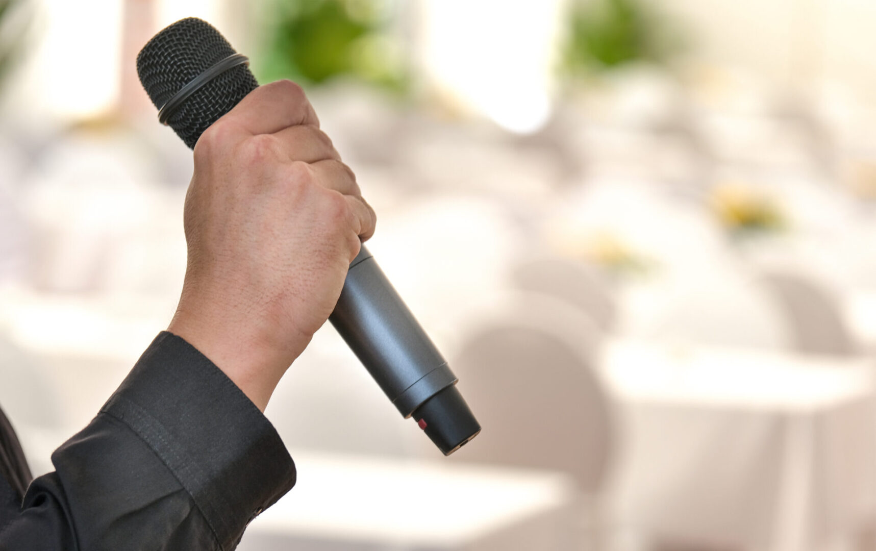 Man holding a black microphone during an event in a decorated banquet hall or ballroom
