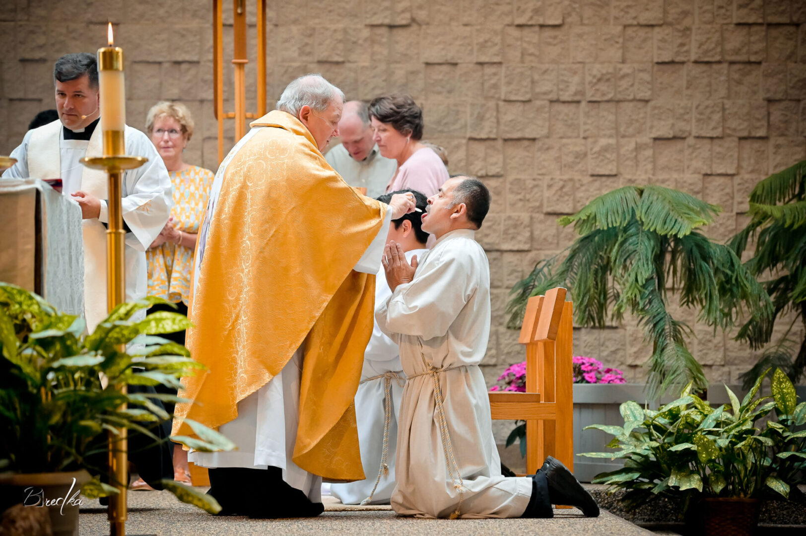 Priest blessing kneeling man during ceremony.