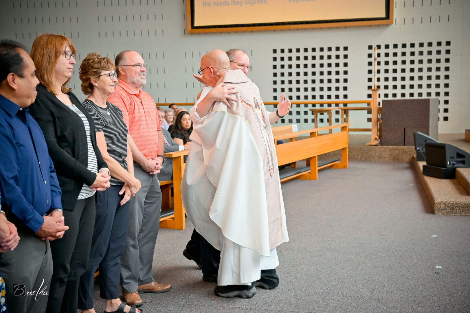 Man in white robe receives a hug in church.
