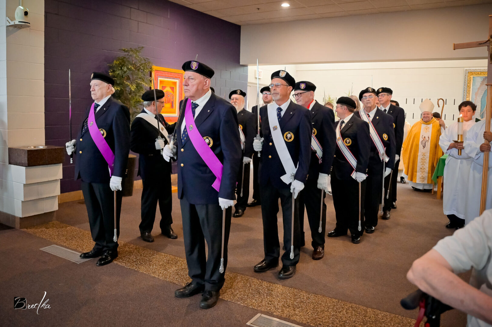 Men in uniform holding swords in procession.
