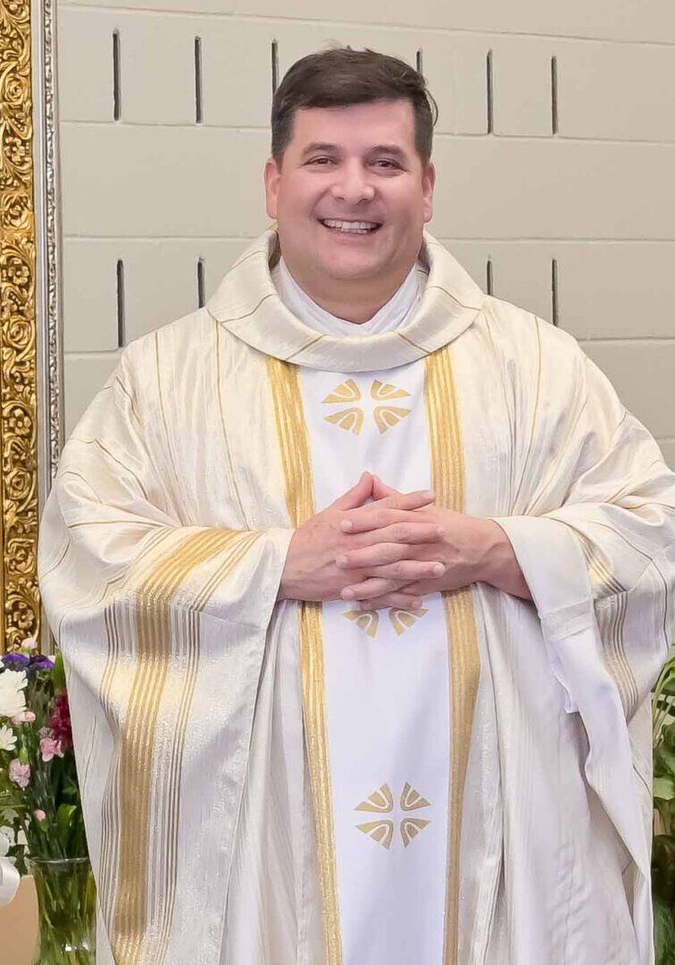 Smiling priest in white robes with gold trim.